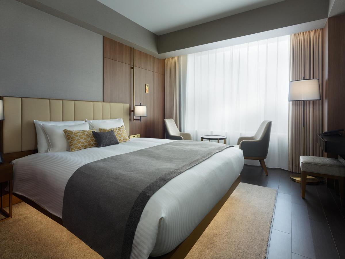 Mitsui Garden Hotel Roppongi Tokyo Premier Eksteriør bilde The photo shows a modern hotel room featuring a large bed with a neatly arranged white and gray bedding. The headboard is upholstered in a light color, adding to the room's contemporary design. On either side of the bed, there are bedside lamps provi