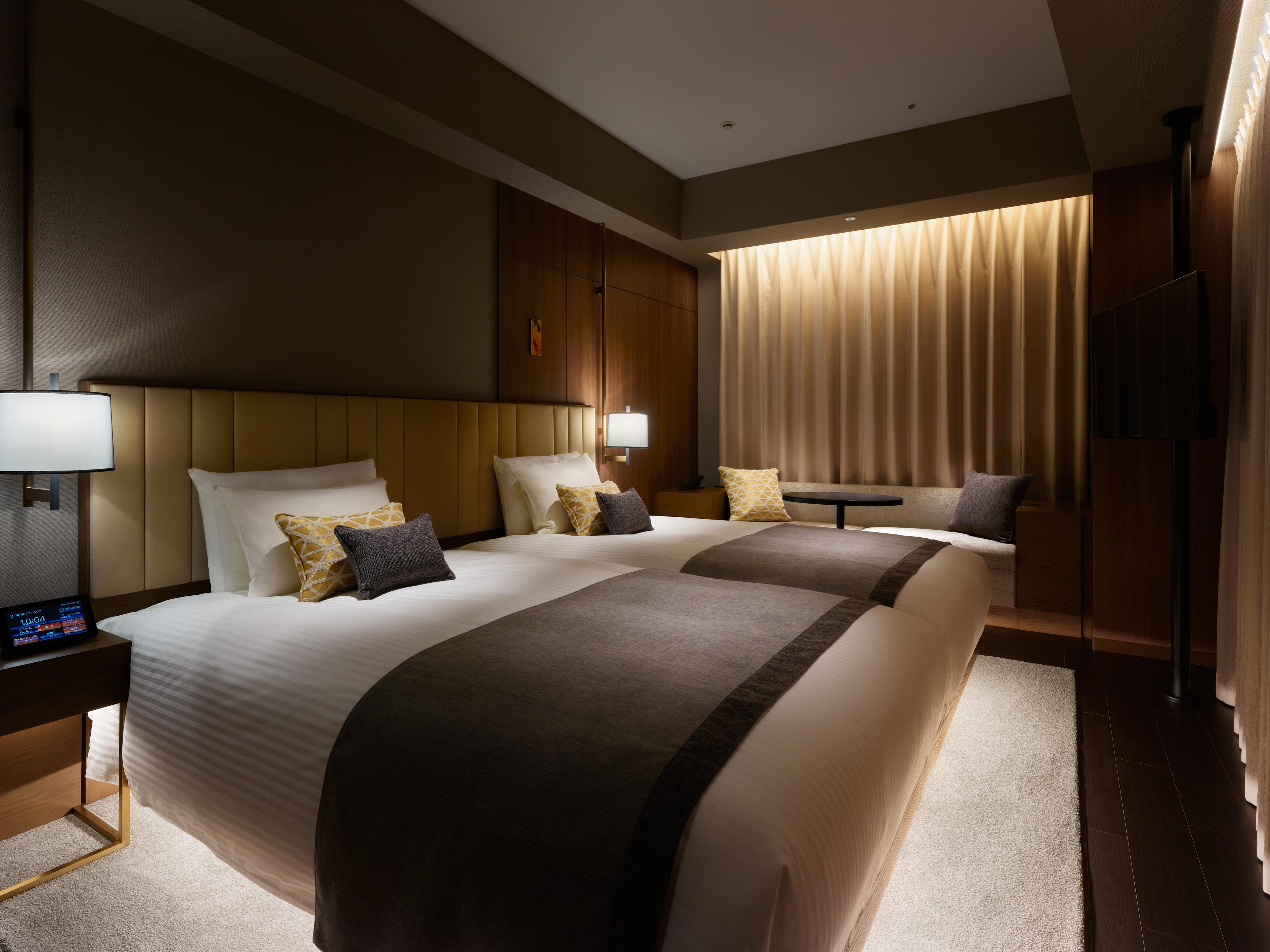 Mitsui Garden Hotel Roppongi Tokyo Premier Eksteriør bilde The photo shows a modern hotel room featuring two beds with plush white linens and decorative pillows. The room has a warm and inviting ambiance, highlighted by soft lighting from lamps and the backlit curtains. There is also a small table with chair