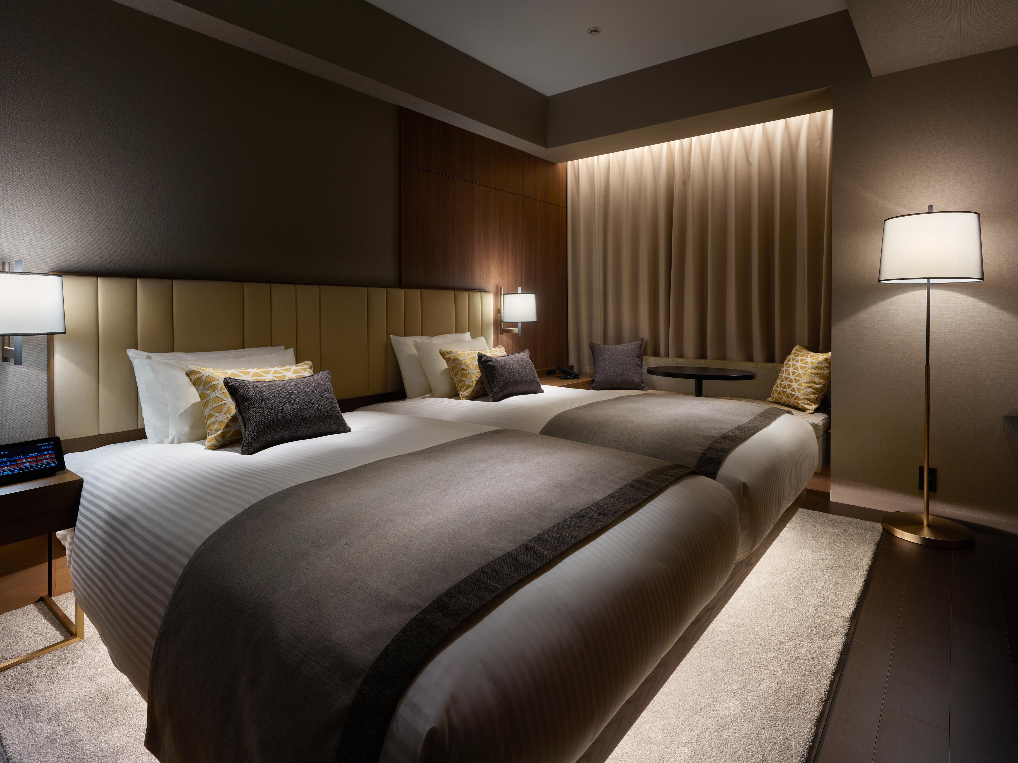 Mitsui Garden Hotel Roppongi Tokyo Premier Eksteriør bilde The photo shows a modern hotel room featuring two beds with elegant bedding in neutral colors. Each bed is adorned with decorative pillows. The room has a sophisticated ambiance with dim lighting, highlighted by table lamps on either side of the beds