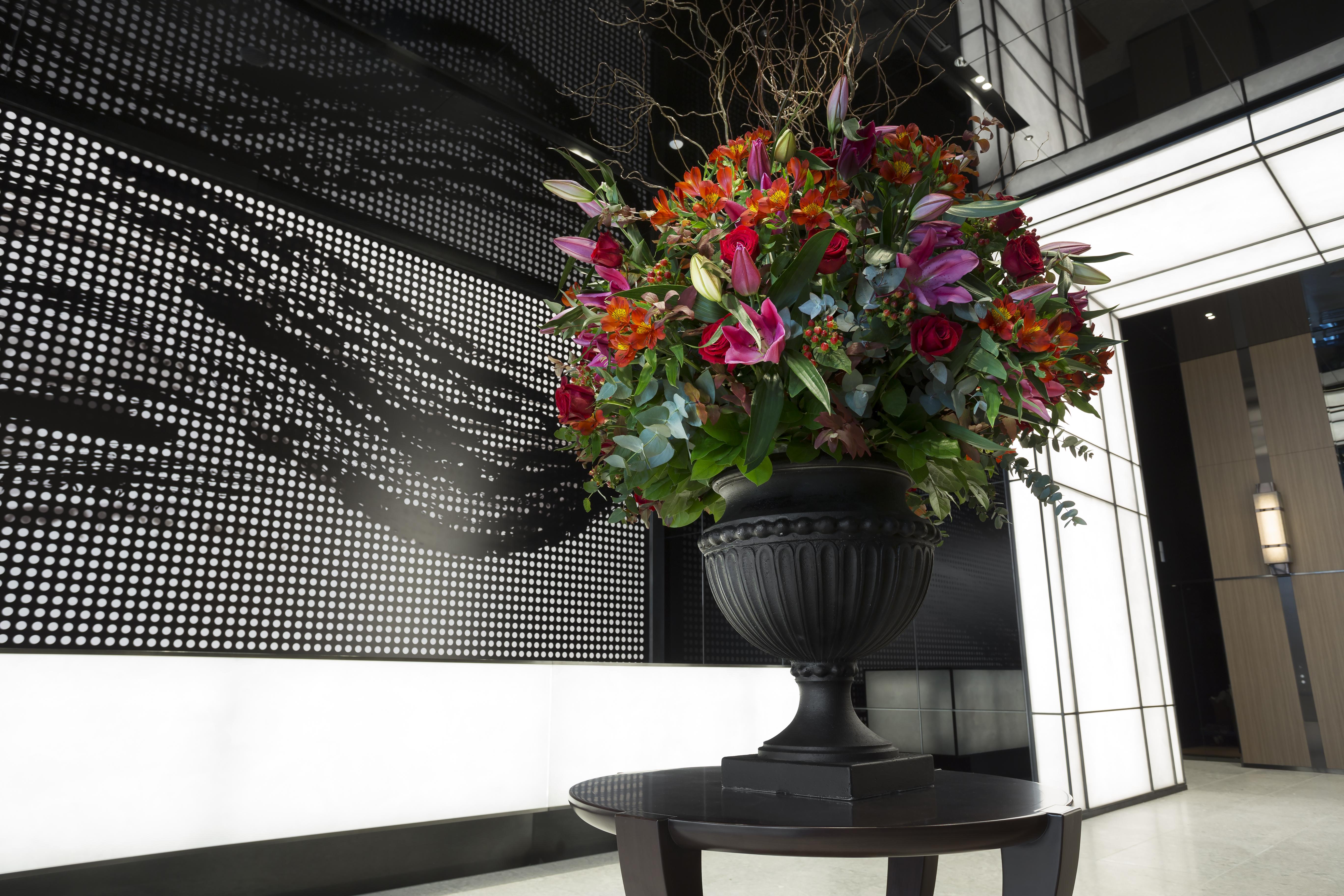 Mitsui Garden Hotel Roppongi Tokyo Premier Eksteriør bilde The photo features a large, vibrant floral arrangement in an ornate black urn. The arrangement is composed of various colorful flowers and greenery, showcasing shades of red, pink, orange, and green. This floral display is positioned on a small table