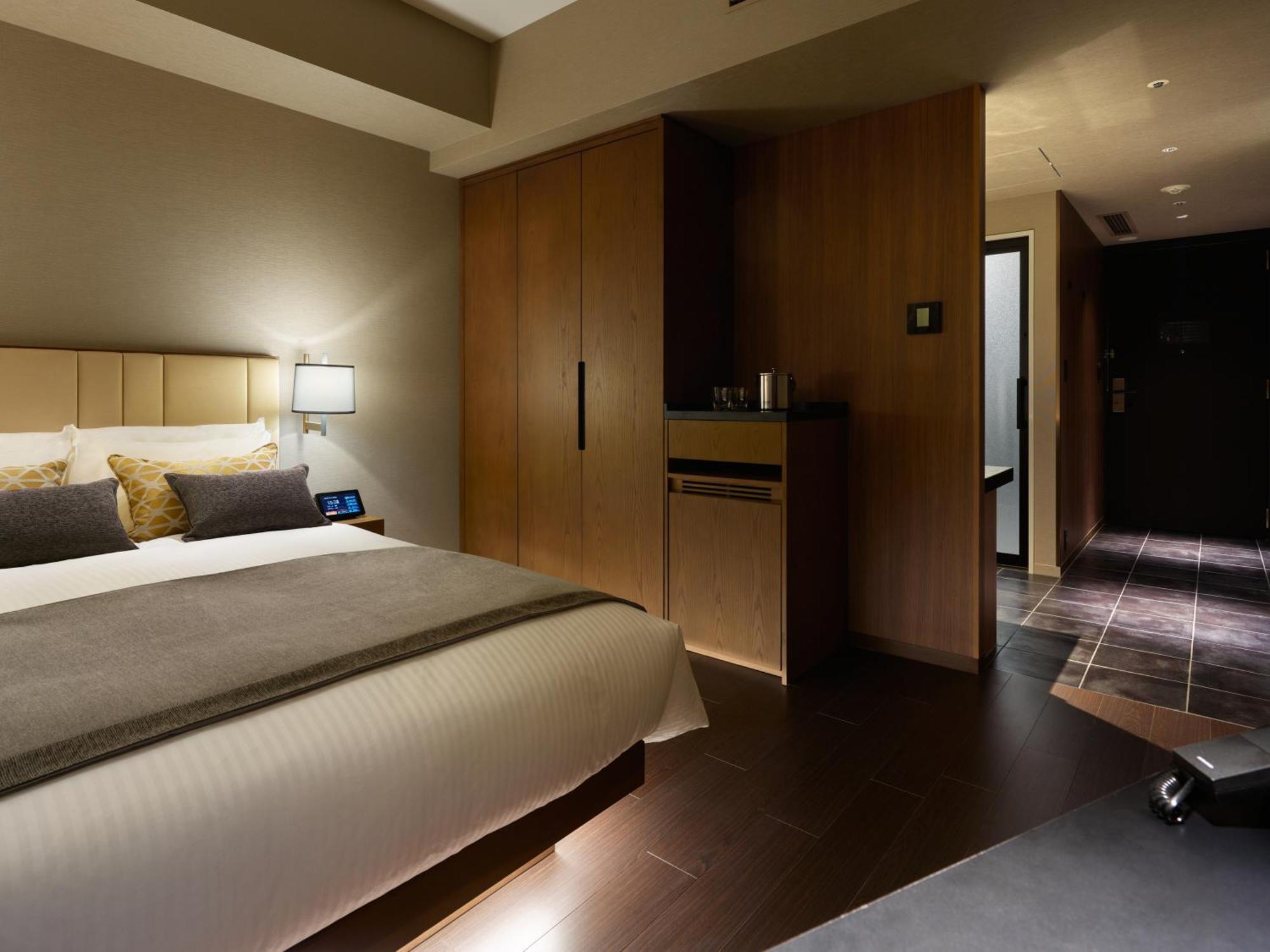 Mitsui Garden Hotel Roppongi Tokyo Premier Eksteriør bilde The photo shows a modern hotel room featuring a neatly made bed with decorative pillows. The room has wooden accents, including a wardrobe and cabinetry, contributing to a warm ambiance. A bedside lamp is on one side of the bed, and there's a small a
